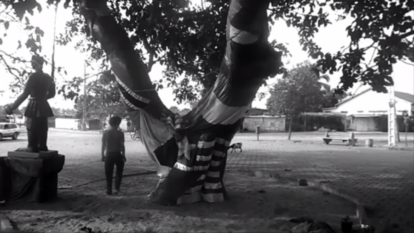 Frame da vídeo performance ‘’L’Arbre D’Oublier’’, de Paulo Nazareth, em que o artista brasileiro, andando de costas, dá 437 voltas na Árvore do Esquecimento. 2013. (1)